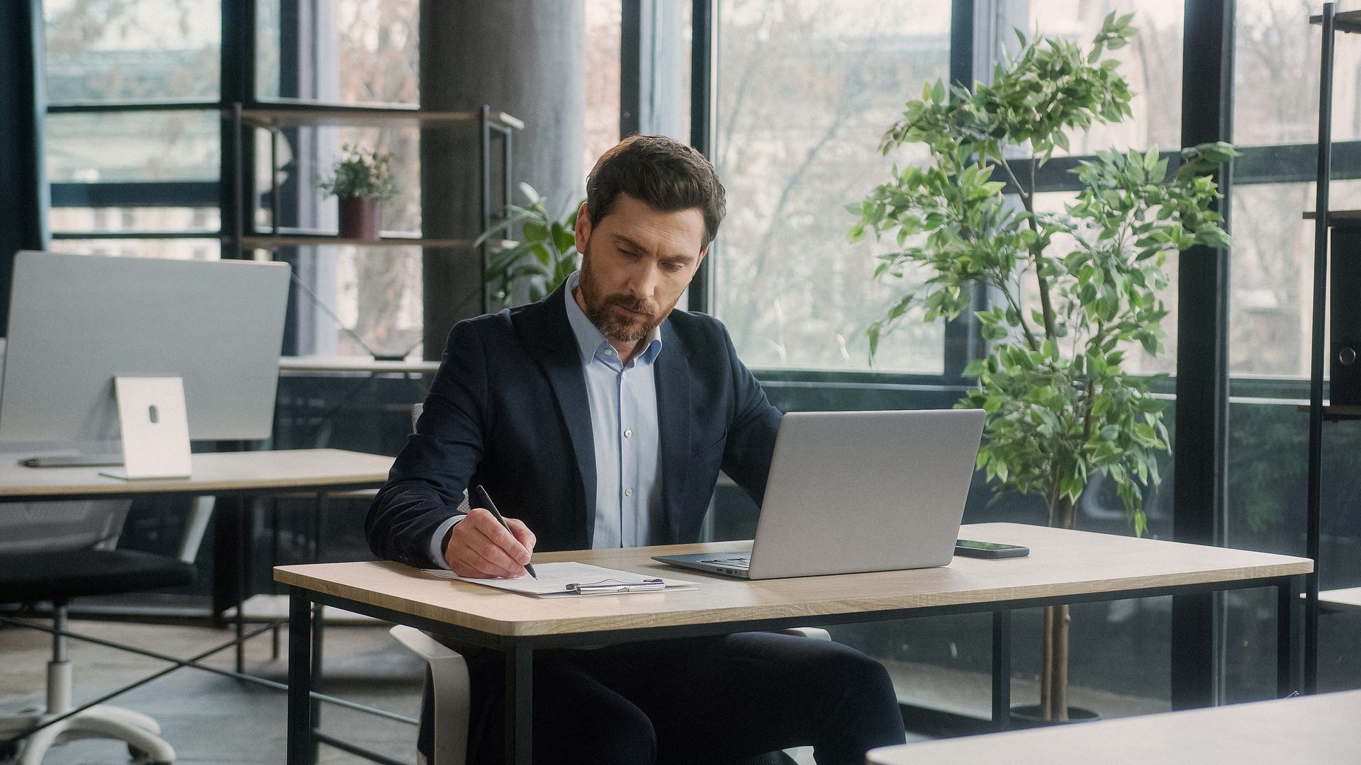 Advisor writing notes at a desk beside a laptop