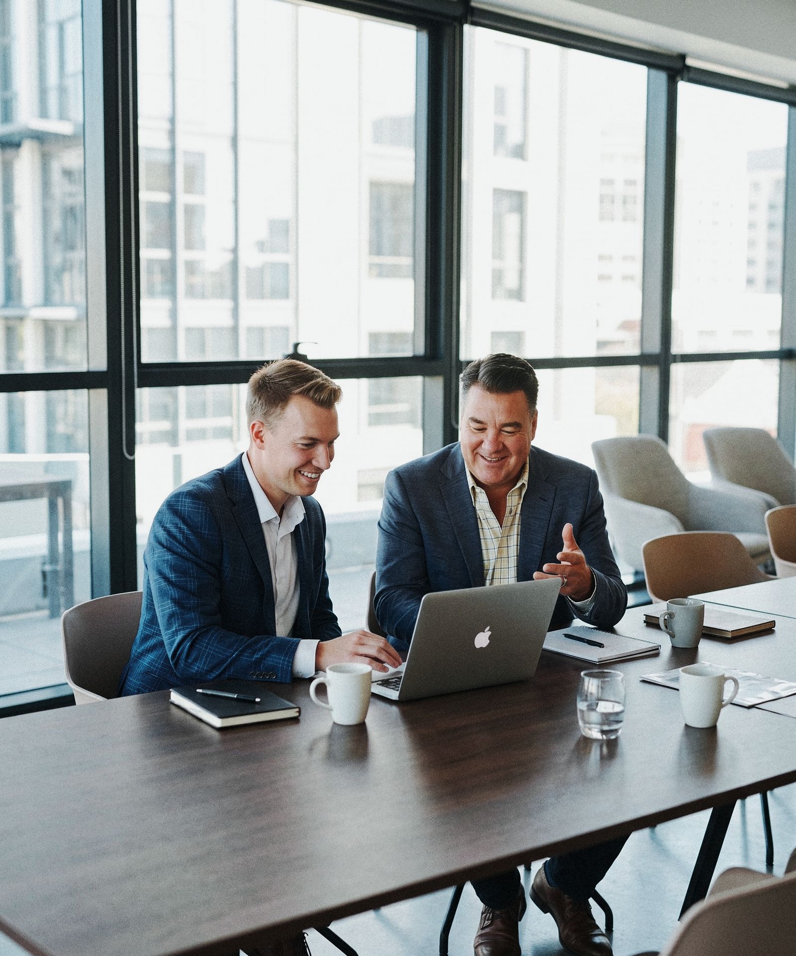Two advisors smiling while reviewing a plan on a laptop