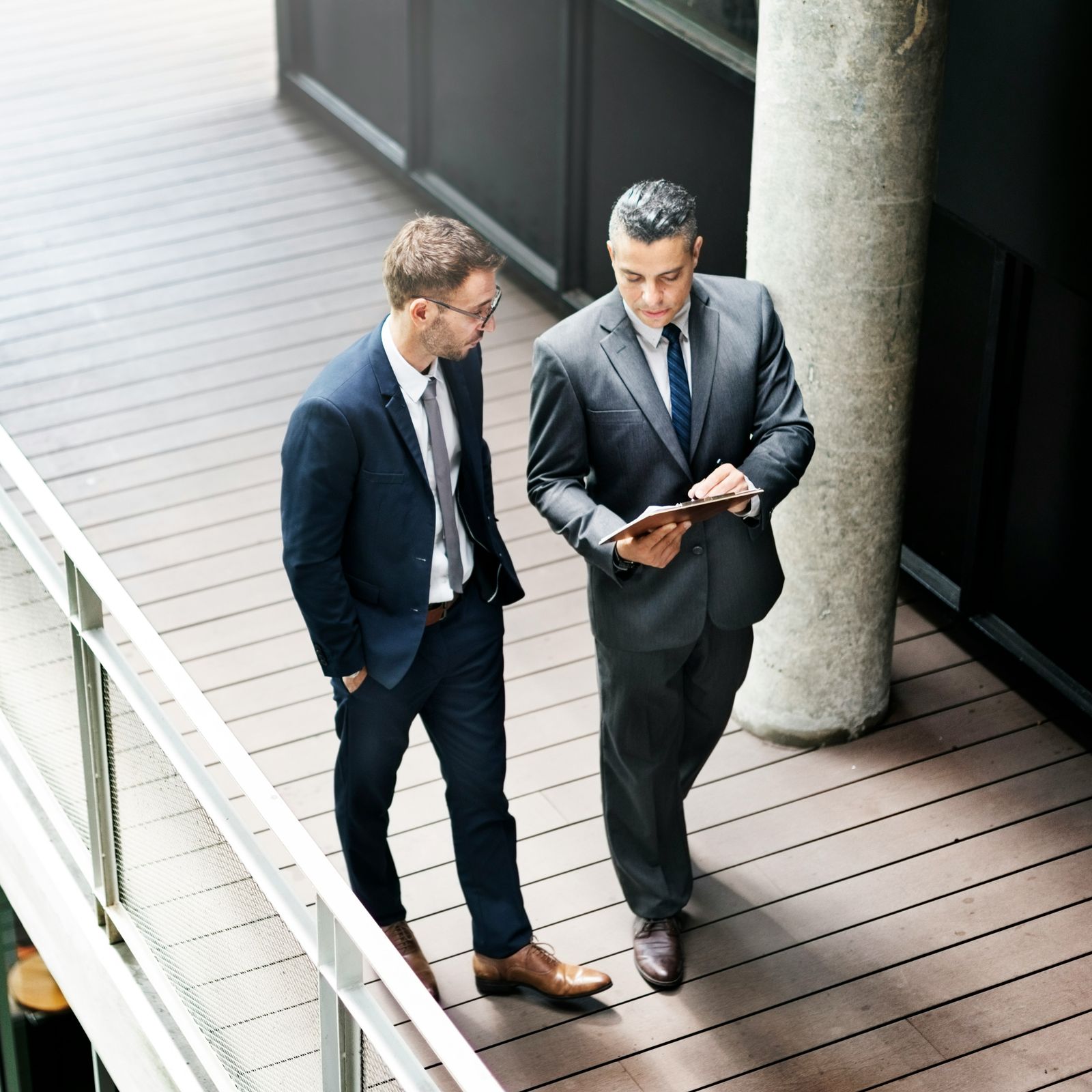 Two business partners in suits talking as they walk along a terrace